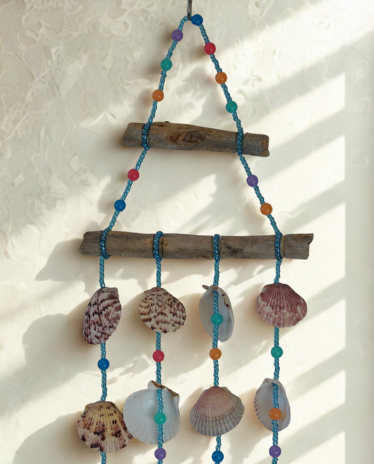 Decorative wall hanging with shells, beads, and driftwood on a light background