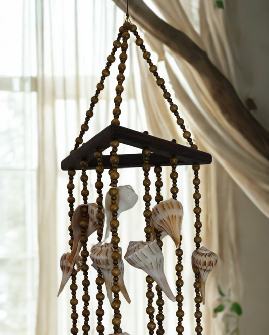 Decorative wind chime with shells hanging against a light curtain background